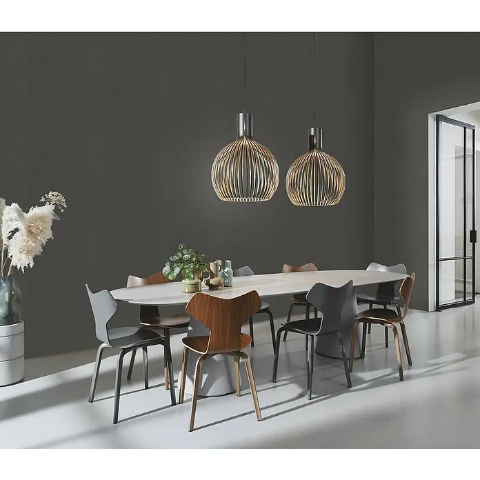 Rasch Color your life Vliestapete Struktur-Uni - Anthrazit, Uni, 10,05 x 0,53 m - Ein stilvolles Esszimmer mit einem ovalen Tisch, umgeben von Designerstühlen, und zwei auffälligen Pendelleuchten, die eine warme Atmosphäre schaffen.