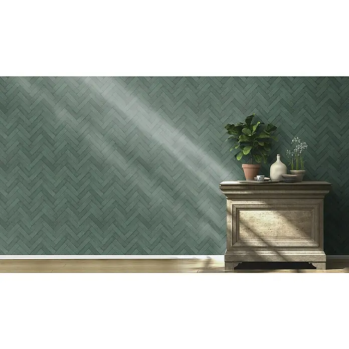 Rasch Factory V Vliestapete Bricks - Flaschengrün, Steinoptik, 10,05 x 0,53 m - Ein stimmungsvolles Interieur mit einer antiken Kommode, Pflanzen und Geschirr vor einer grünen, gemusterten Wand im Fischgrätmuster.