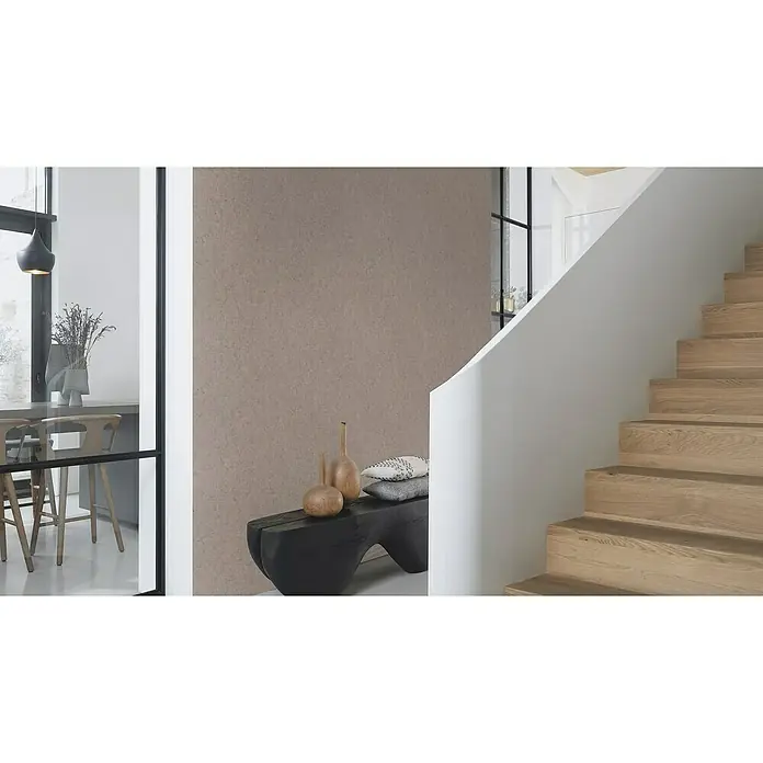 Rasch Factory V Vliestapete Beton-Uni - Taupe dunkel, Uni, 10,05 x 0,53 m - Eine Nahaufnahme einer Wand mit einer texturierten Oberfläche, die eine subtile und elegante Ästhetik präsentiert. Die Farbgebung ist neutral gehalten.