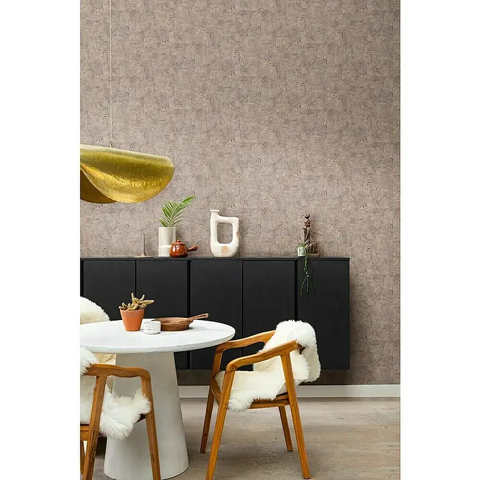 Rasch African Queen III Vliestapete Holz - Dunkelbeige, Holzoptik, 10,05 x 0,53 m - Stilvolles Esszimmer mit einem runden Tisch, Holzstühlen mit Fellauflagen und einer goldenen Hängelampe vor einer gemusterten Tapete.
