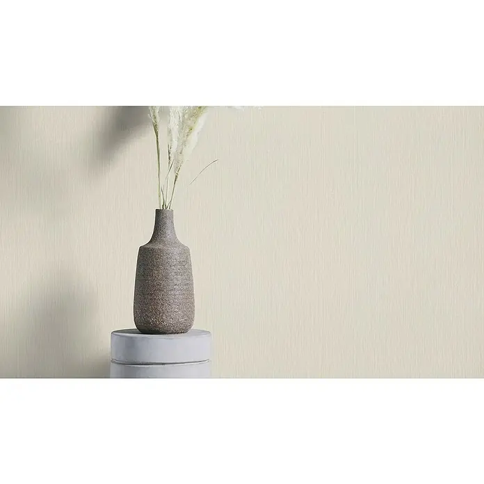 Rasch Country Charme Vliestapete Textil-Uni - Lichtgrau, Uni, 10,05 x 0,53 m - Dekoratives Stillleben mit einer Vase und Trockenblumen auf einem runden Sockel vor einer hellen Wand.