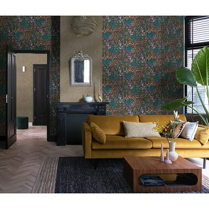 Rasch Curiosity Vliestapete Pflanzen - Offblack, Floral, 10,05 x 0,53 m - Ein elegantes Wohnzimmer mit einer senffarbenen Samtcouch, floraler Tapete und einem dunklen Holztisch, der einen Hauch von Luxus verleiht.
