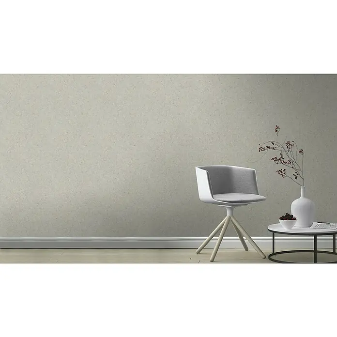 Rasch Factory V Vliestapete Beton-Uni - Hellgrau, Uni, 10,05 x 0,53 m - Elegantes Interieur mit einem modernen Stuhl, einem Beistelltisch mit Dekorationen und einer stilvollen Vase, alles vor einer dezenten Wand.