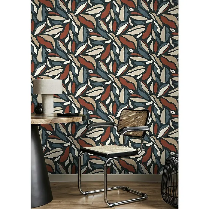 Rasch Symphony Vliestapete Muster - Rostrot, Grafisch, 10,05 x 0,53 m - Detailaufnahme eines Innenraums mit floral gemusterter Tapete, Tisch mit Lampe und einem Stuhl mit Rohrgeflecht.