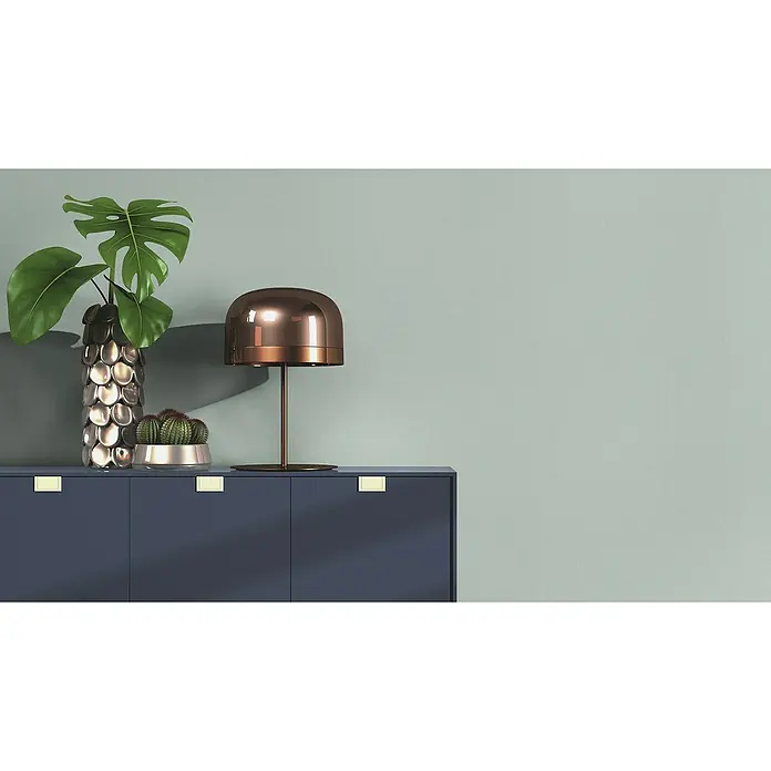 Rasch Wall Textures VI Vliestapete Textil-Uni - Hellblau, Uni, 10,05 x 0,53 m - Elegantes Sideboard in Dunkelblau mit minimalistischen Goldgriffen, dekoriert mit einer Monstera-Pflanze, einem Kaktus und einer modernen Lampe.