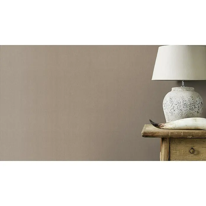 Rasch Color your life Vliestapete Uni-Struktur - Mittelbraun, Uni, 10,05 x 0,53 m - Eine elegante Tischleuchte mit cremefarbenem Schirm und rustikalem Fuß auf einem Beistelltisch, die eine warme Atmosphäre schafft.