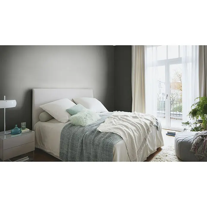 Rasch Wall Textures VI Vliestapete Struktur-Uni - Anthrazit, Uni, 10,05 x 0,53 m - Helles Schlafzimmer mit großem Bett, weicher Bettwäsche und einem Nachttisch mit Lampe. Der Raum ist freundlich und einladend gestaltet.