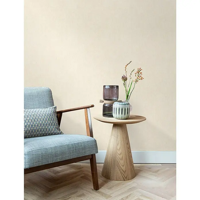 Rasch Wall Textures VI Vliestapete Struktur-Uni - Braunbeige, Uni, 10,05 x 0,53 m - Eine stilvolle Einrichtungsszene mit einem grauen Sessel, einem Holztisch mit Dekoration und einem Vasenensemble.