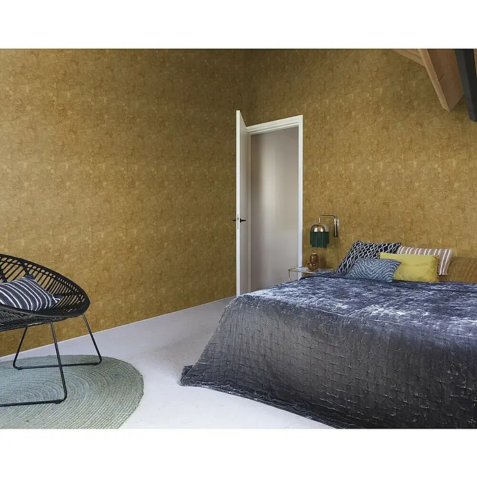 Rasch Factory V Vliestapete Uni-Struktur - Gold, Wellen, 10,05 x 0,53 m - Schlafzimmer mit einem gemütlichen Doppelbett, einem eleganten Sessel und einer stilvollen Wandlampe für eine entspannte Atmosphäre.