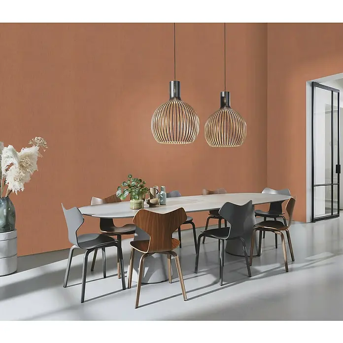 Rasch Color your life Vliestapete Uni-Struktur - Terra, Uni, 10,05 x 0,53 m - Ein Esszimmer mit einem weißen ovalen Tisch, umgeben von Stühlen und beleuchtet von zwei modernen Pendelleuchten.