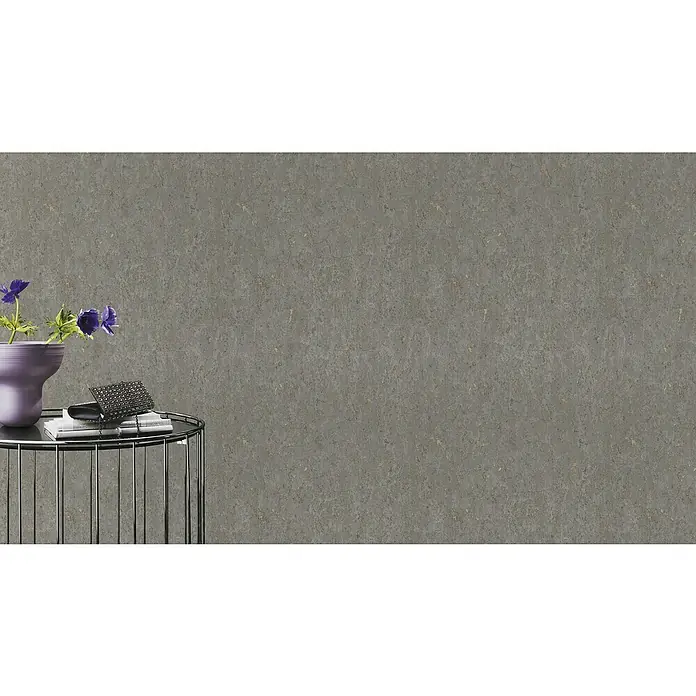 Rasch Curiosity Vliestapete Kork-Optik - Dunkelgrau, Steinoptik, 10,05 x 0,53 m - Nahaufnahme eines kleinen Beistelltisches mit Blumen, Büchern und einer verzierten Handtasche vor einer grauen Wand.