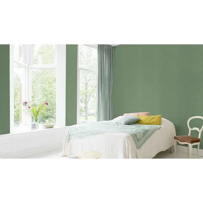 Rasch Color your life Vliestapete Uni-Struktur - Mittelgrün, Uni, 10,05 x 0,53 m - Ein helles Schlafzimmer mit einem gemütlichen Bett, dekoriert mit Kissen und einer Tagesdecke, sowie einem Fenster mit üppigem Grün im Hintergrund.