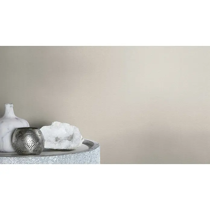 Rasch Country Charme Vliestapete Textil-Uni - Hellgrau, Uni, 10,05 x 0,53 m - Nahaufnahme einer dekorativen Komposition mit einer weißen Marmorvase, einem silbernen Windlicht und einem weißen Kristall auf einem verzierten Tisch.