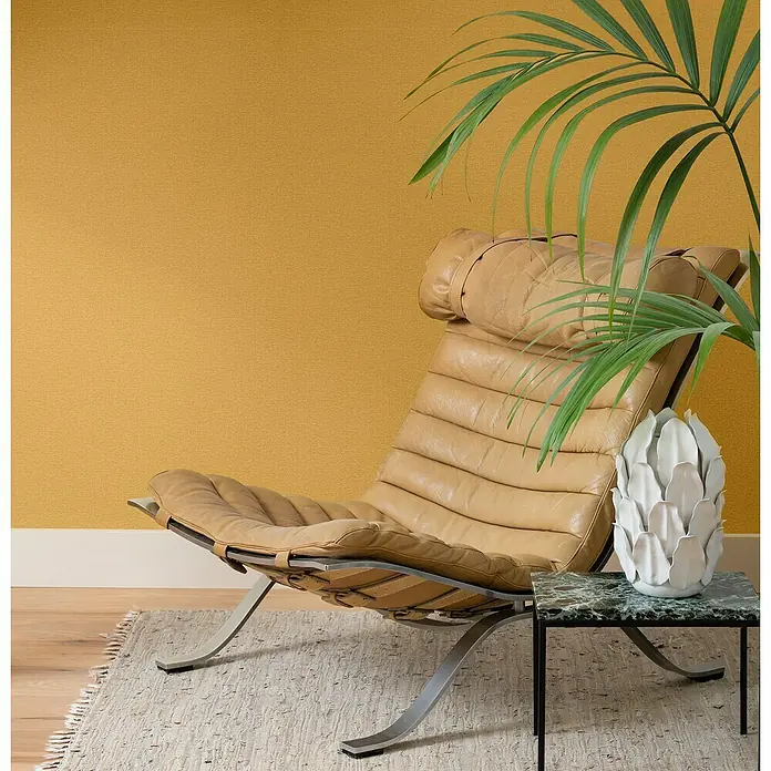 Rasch Wall Textures VI Vliestapete Leinen-Uni - Ocker, Uni, 10,05 x 0,53 m - Ein bequemer Ledersessel mit Kopfstütze, der zum Entspannen einlädt, kombiniert mit einem stilvollen Beistelltisch und einer dekorativen Vase.