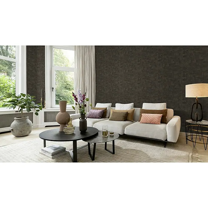 Rasch African Queen III Vliestapete Holz - Schwarzbraun, Holzoptik, 10,05 x 0,53 m - Wohnzimmer mit einem hellen Sofa, dunklem Couchtisch und einer Stehlampe auf einem Beistelltisch. Die Wand ist dunkel gemustert.