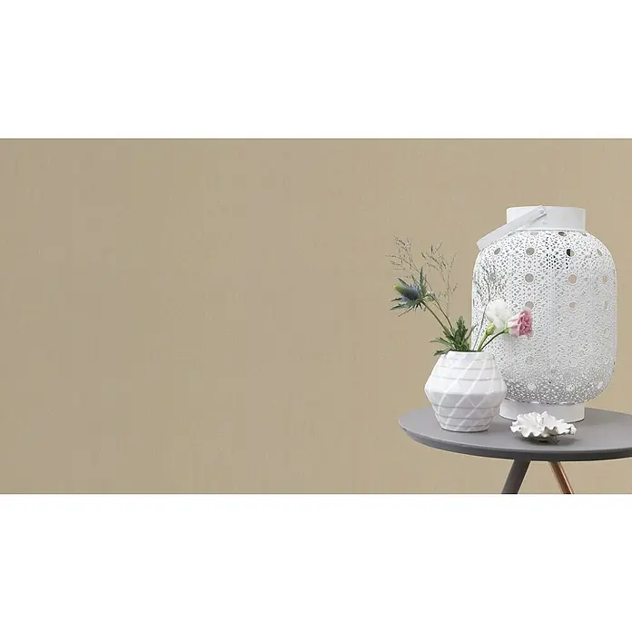 Rasch Color your life Vliestapete Struktur-Uni - Creme dunkel, Uni, 10,05 x 0,53 m - Nahaufnahme eines weißen Windlichts neben einer kleinen Vase mit Blumen auf einem grauen Tisch.