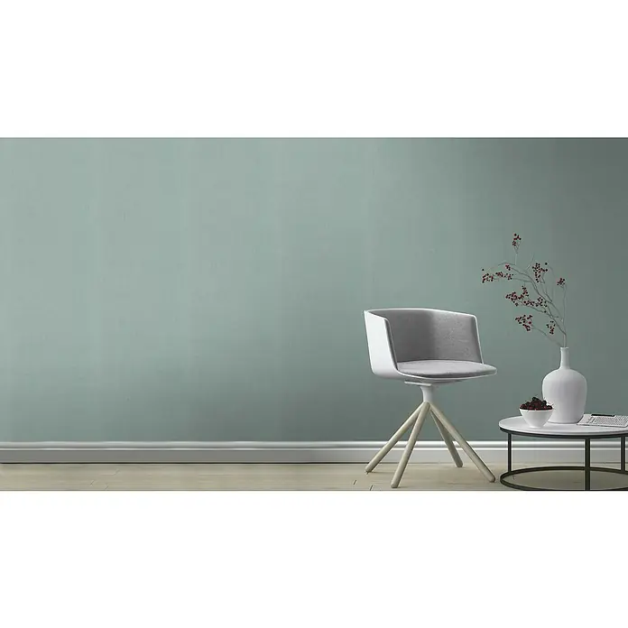 Rasch Color your life Vliestapete Struktur-Uni - Helltürkis, Uni, 10,05 x 0,53 m - Ein moderner grauer Stuhl mit einem weißen Gestell steht neben einem Tisch mit Dekoration vor einer mintgrünen Wand.