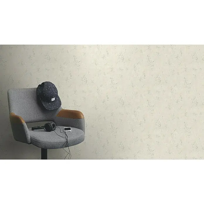 Rasch Color your life Vliestapete Uni-Struktur - Hellbeige, Steinoptik, 10,05 x 0,53 m - Ein grauer Drehstuhl mit Armlehnen, auf dem eine Mütze, Kopfhörer und ein kleiner Bildschirm liegen, vor einem beigen Hintergrund.