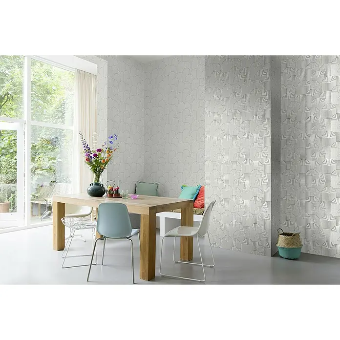 Rasch Color your life Vliestapete Retro - Graubeige, Grafisch, 10,05 x 0,53 m - Innenaufnahme eines Raumes mit stilvoller Tapete mit Art-Deco-Muster, einem Holztisch und farbenfrohen Akzenten.