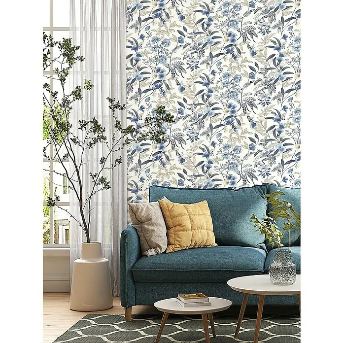 Rasch Symphony Vliestapete Blumen - Hellblau, Floral, 10,05 x 0,53 m - Elegantes Wohnzimmer mit blauem Sofa, floraler Tapete, hellen Kissen und Holztischen auf einem gemusterten Teppich.