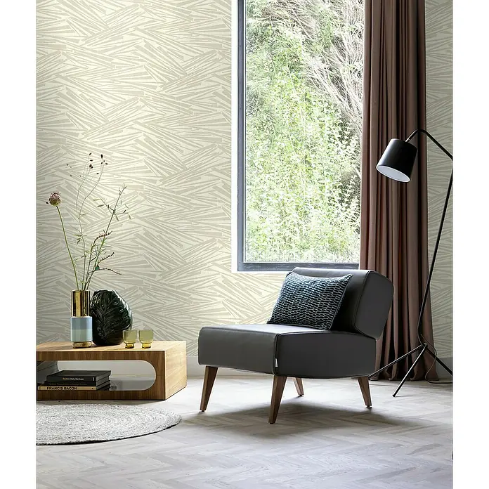 Rasch Sky Lounge Vliestapete Mikado - Perlmutt, Grafisch, 10,05 x 0,53 m - Elegantes Interieur mit einem grauen Sessel, einem Holztisch mit Dekoration und einer Stehlampe vor einer gemusterten Tapete.
