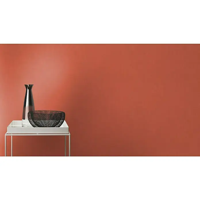 Rasch Wall Textures VI Vliestapete Uni - Rostrot, Uni, 10,05 x 0,53 m - Schlichte Deko: Eine elegante, dunkle Vase und eine dekorative Schale auf einem weißen Tisch vor einem terracottafarbenen Hintergrund.