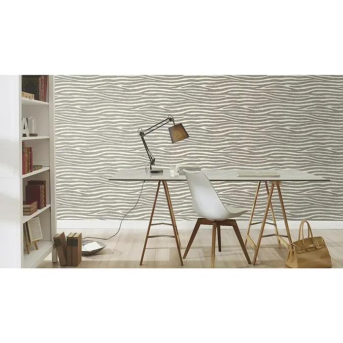 Rasch African Queen III Vliestapete Zebrafell - Hellgrau, Tieroptik, 10,05 x 0,53 m - Eine elegante Büroeinrichtung mit einem minimalistischen Schreibtisch, einer modernen Lampe und einem stilvollen Bücherregal vor einer wellenförmigen Tapete.
