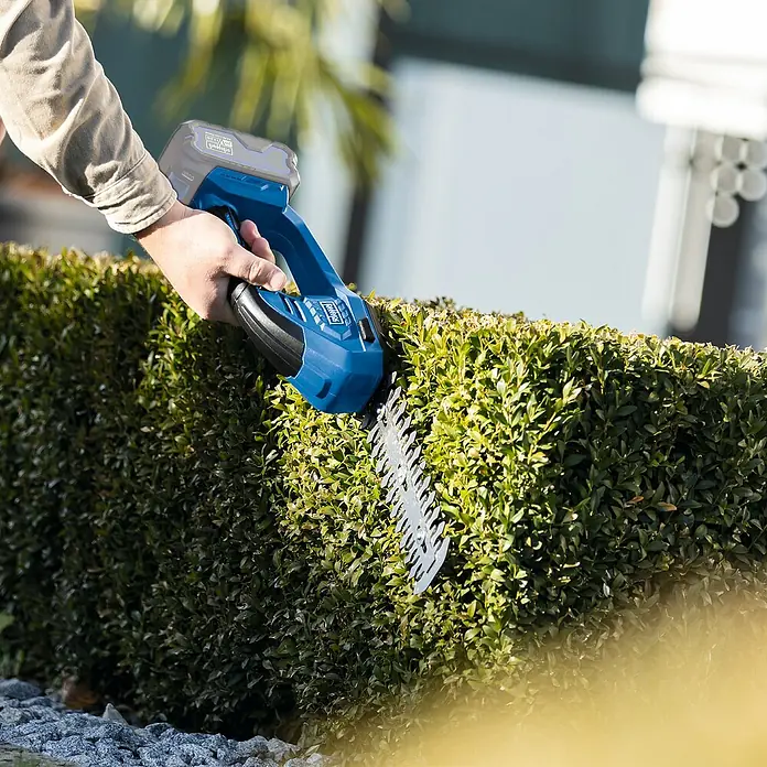 Scheppach IXES 20V Akku-Gras- & Strauchschere C-HTGS200-X - Li-Ionen, Ohne Akku, Schwertbreite: 90 mm - Ein Mann schneidet eine Hecke mit einer akkubetriebenen Heckenschere von Scheppach, die für präzise Gartenarbeit sorgt.