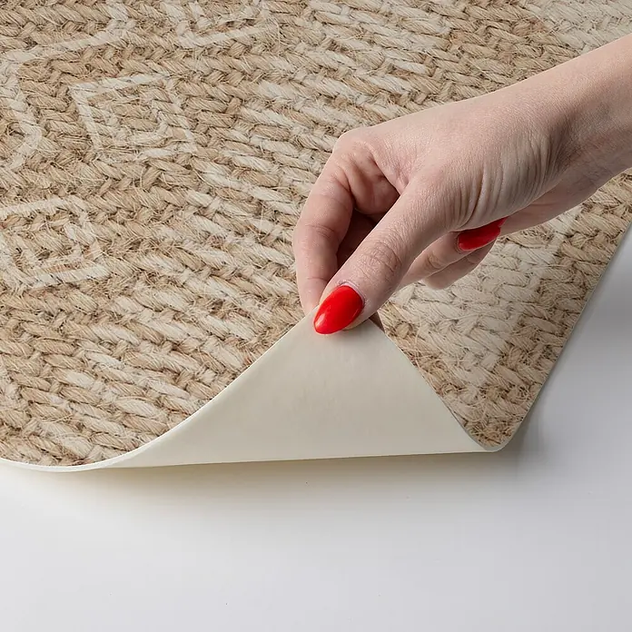 Alfombra de vinilo Telma - Natural, 75 x 48 cm, PVC - Primer plano de una baldosa de vinilo autoadhesiva con un patrón de tejido de yute, que está siendo despegada por una mano con uñas rojas.