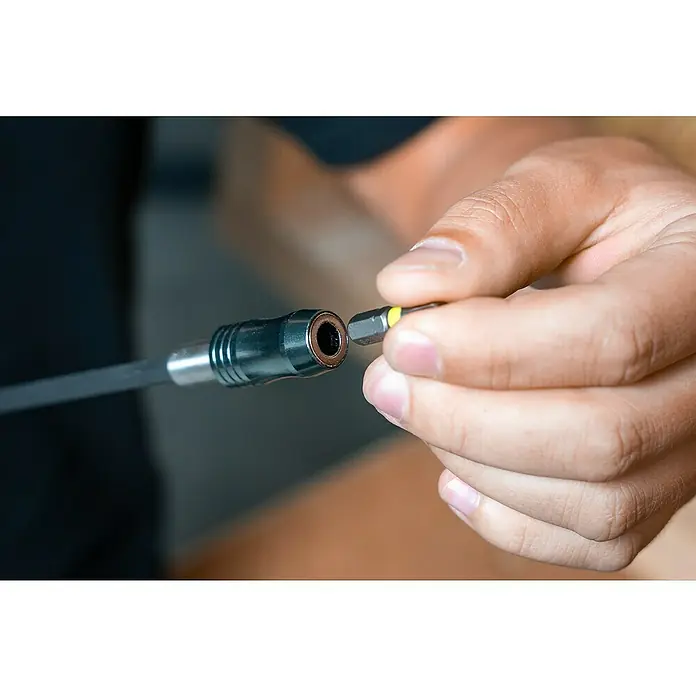 Wolfcraft Bithalter250 mm, Ringmagnet - Detailaufnahme einer Hand, die einen gelben Schraubendreheraufsatz in eine magnetische Bitverlängerung einführt.