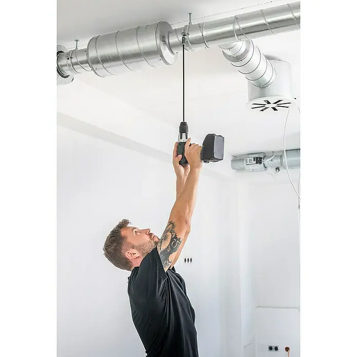 Wolfcraft Bithalter - Länge: 450 mm - Mann, der mit einem Akkuschrauber an einer Lüftungsanlage arbeitet, um diese zu befestigen. Er trägt ein schwarzes T-Shirt und hat Tattoos auf dem Arm.