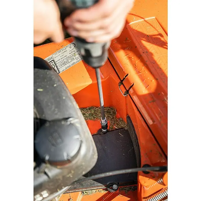 Wolfcraft Bithalter250 mm, Ringmagnet - Ein Akku-Bohrschrauber mit einer langen Verlängerung, der verwendet wird, um eine orangefarbene Rasenmäherkomponente zu befestigen.