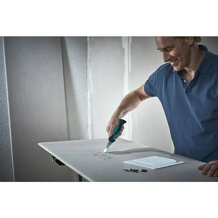 Wolfcraft Gipskartonplatten-Stichsäge - Geeignet für: Gipskartonplatten - Mann schneidet mit einer Säge in eine Gipskartonplatte, daneben ein Lüftungsgitter und Schrauben.