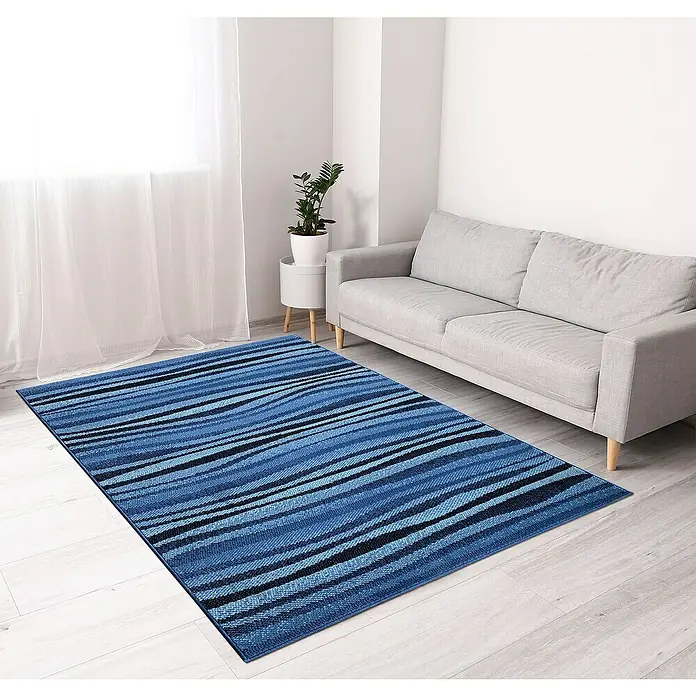 Alfombra de pelo corto Ondas - Azul, 170 x 120 cm, Polipropileno - Una alfombra azul de rayas se encuentra en una sala de estar luminosa con un sofá y una ventana. La alfombra es el foco de la habitación.