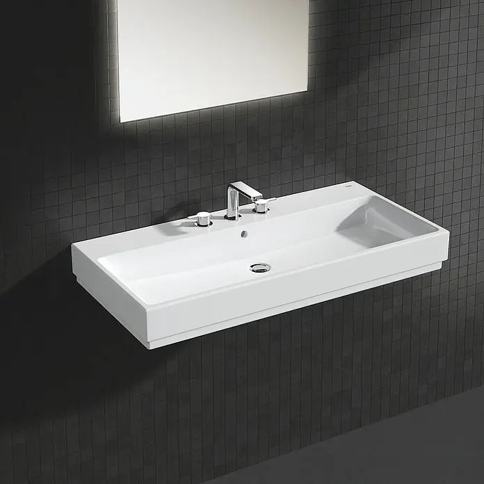 Grohe Lineare Waschtischarmatur - 3-Loch, Chrom, Glänzend - Moderne Waschbecken-Einheit mit rechteckigem, weißem Becken, Armatur und beleuchtetem Spiegel vor dunklem Fliesenhintergrund.