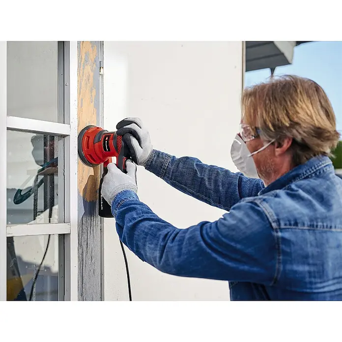 Einhell Classic Elektro-Exzenterschleifer TC-RS 425 E - 425 W, Durchmesser Schleifteller: 125 mm - Mann benutzt einen Einhell Exzenterschleifer zum Abschleifen eines Fensterrahmens, mit Schutzmaske und Brille.