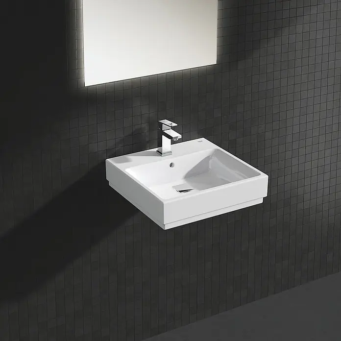 Grohe Eurocube Waschtischarmatur S-Size - Chrom, Glänzend, Mit Zugstange, Mit Durchflussbegrenzung - Moderne Waschbecken-Garnitur: ein quadratisches, wandmontiertes Waschbecken mit Chromarmatur und Spiegel vor einem dunkelgrauen Mosaikhintergrund.