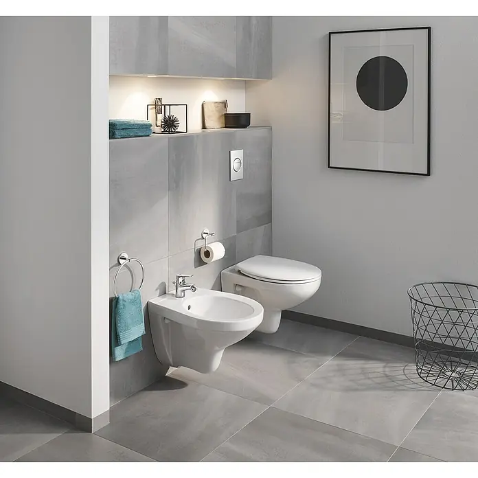 Grohe BauFlow Bidetarmatur - Chrom, Glänzend - Ein elegantes Badezimmer mit einer wandmontierten Toilette und einem Bidet, hervorgehoben durch graue Fliesen und moderne Armaturen.