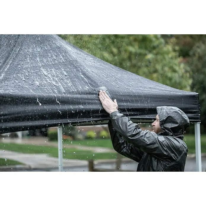 T-Rex Reparaturband Waterproof Tape - Schwarz, 1,5 m x 50 mm - Ein Mann in Regenkleidung berührt ein schwarzes Zelt, auf dem sich Wassertropfen befinden. Das Zelt schützt vor dem Regenwetter.