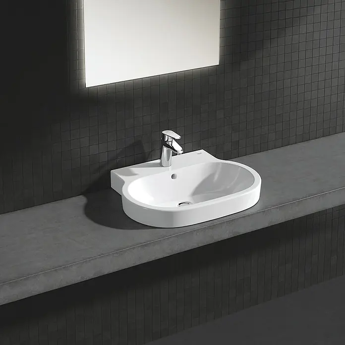 Grohe Eurodisc Cosmopolitan Waschtischarmatur S-Size mit Energiesparfunktion - Mit Zugstange, Chrom, Glänzend - Nahaufnahme eines modernen Waschbeckens mit Armatur auf einer grauen Arbeitsplatte vor einer dunklen, gekachelten Wand und einem beleuchteten Spiegel.