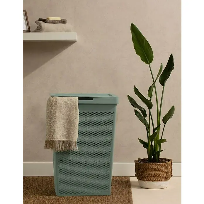 Tatay Bohol Cesta para la ropa - L x An x Al: 42,5 x 35,5 x 62 cm, Verde Sage - Una cesta de lavandería color menta con tapa y una toalla beige colgando en el lateral, junto a una planta verde en una maceta.