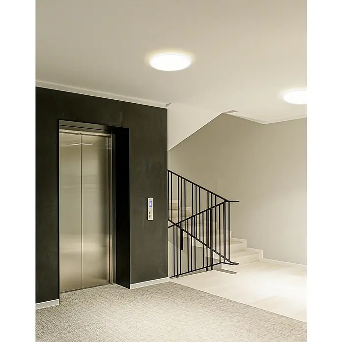 Eglo LED-Deckenleuchte Minerario - 20,2 W, Ø x H: 39 x 3 cm, Weiß, Warmweiß - Aufzug neben einer Treppe in einem Gebäude. Runde Deckenleuchten beleuchten den Raum, während die Treppe zur nächsten Etage führt.