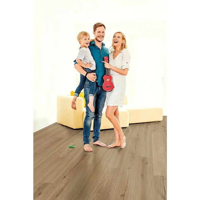 Decolife Designbodenmuster Naturestyle Pure Oak Smoke - 28 x 16 x 9 mm, Landhausdiele, Oak Smoke - Familie steht barfuß auf einem hochwertigen Holzboden. Der Boden verleiht dem Raum eine warme und einladende Atmosphäre und ist ein echter Hingucker.