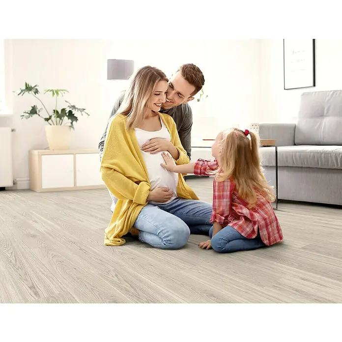 Decolife Designbodenmuster Naturestyle Pure Oak Select White - 28 x 16 x 9 mm, Landhausdiele, Oak Select White - Helles Laminat bildet den Untergrund für eine werdende Familie, die auf dem Boden sitzt und sich auf das kommende Baby freut.