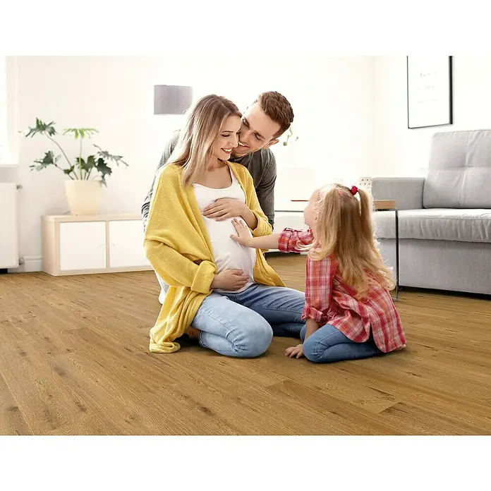 Decolife Designboden Naturestyle Pure - Oak Amber, Landhausdiele, 1.220 x 185 x 9 mm - Glückliche Familie auf warmem Holzfußboden. Mutter erwartet Baby, Vater umarmt sie, Tochter berührt Mamas Bauch.