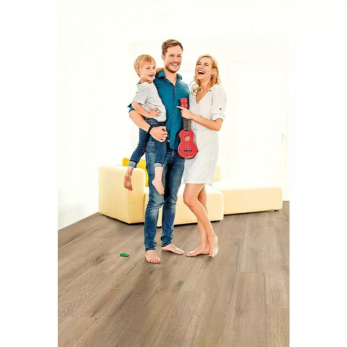 Decolife Designbodenmuster Naturestyle Pure Oak Raw - 28 x 16 x 9 mm, Landhausdiele, Oak Raw - Familie barfuß auf hellem Laminat in natürlicher Holzoptik, das Wärme und Komfort im Zuhause zeigt.