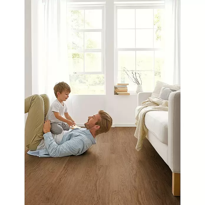 Decolife Designboden Freestyle Access Hazelnut Oak - 1.220 x 185 x 8,5 mm, Landhausdiele, Hazelnut Oak - Brauner Holzfußboden mit natürlicher Maserung, verlegt in einem hellen Wohnzimmer, wo ein Mann und ein Kind spielen.