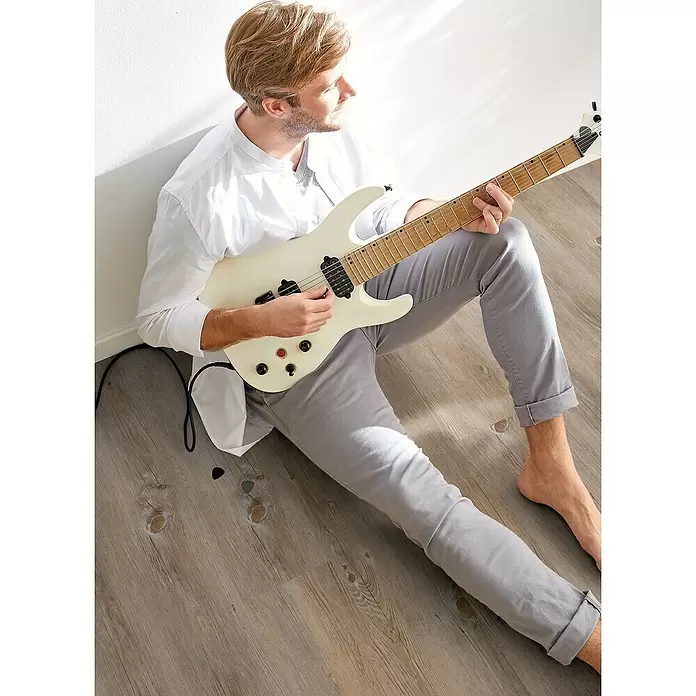 Decolife Designboden Freestyle Access Kenai Oak - 1.220 x 185 x 8,5 mm, Landhausdiele, Kenai Oak - Eine Person sitzt auf dem Boden und spielt eine weiße E-Gitarre.