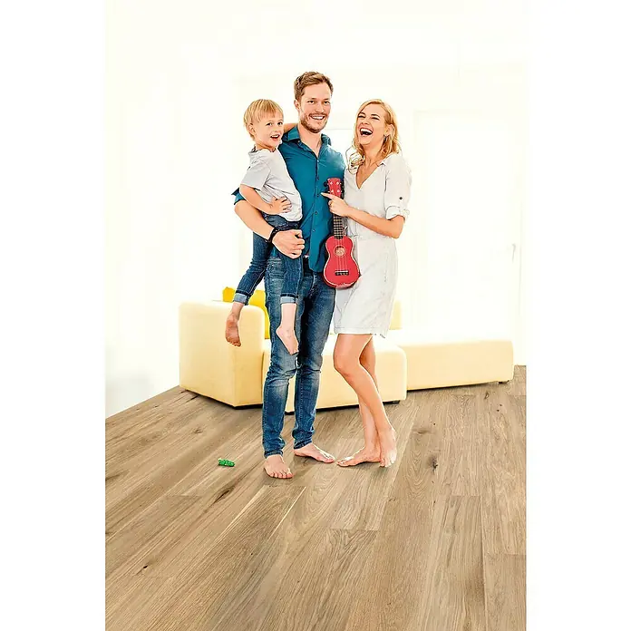 Decolife Designboden Naturestyle Pure - Oak Rustic, Landhausdiele, 1.220 x 185 x 9 mm - Ein glückliches Paar mit Kind auf einem Holzboden. Das helle Parkett sorgt für eine warme Atmosphäre im Raum und betont die Natürlichkeit.