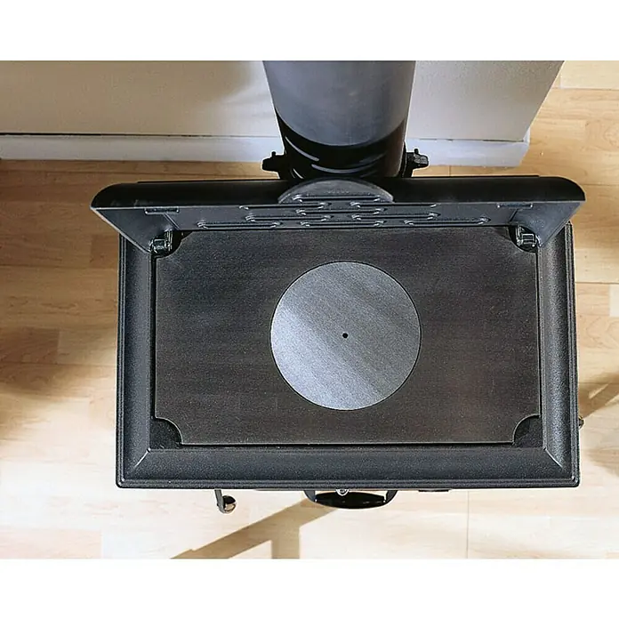 La Nordica Kaminofen Isetta Evo - 9,4 kW, Mit Kochplatte, Raumheizvermögen: 221 m³, Material Verkleidung: Stahl, Schwarz - Detailaufnahme eines schwarzen Kaminofens mit runder Kochplatte. Das Gerät steht auf einem Holzboden und ist teilweise von einer Wand umgeben.